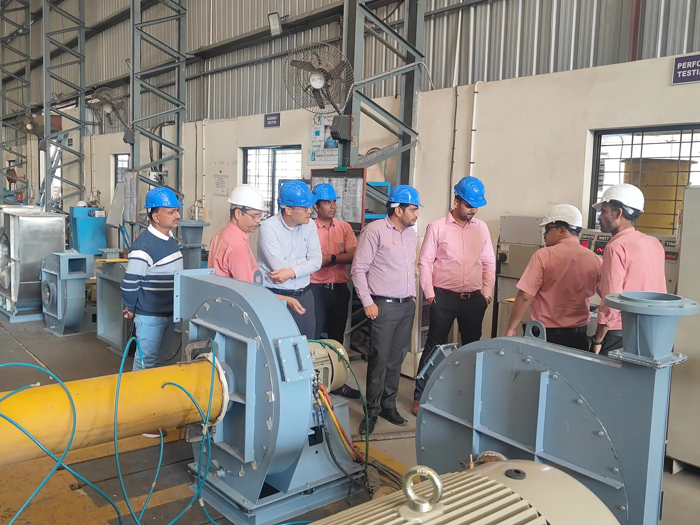 Visiting engineers in hard hats around a centrifugal fan at the performance test bed